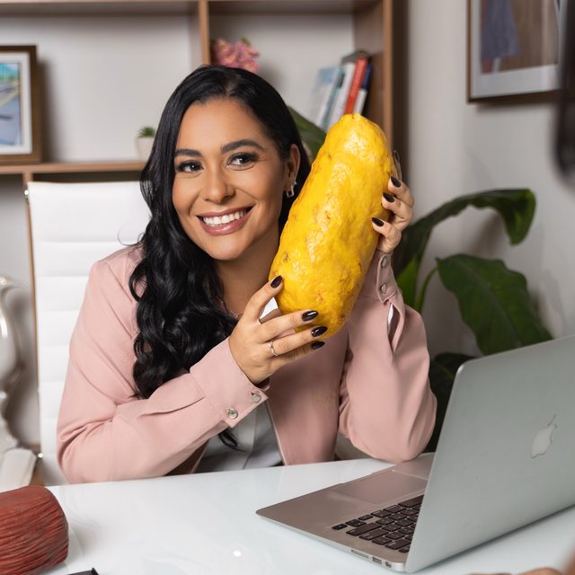 Monique Fahel sorrindo com um modelo de gordura corporal na mão